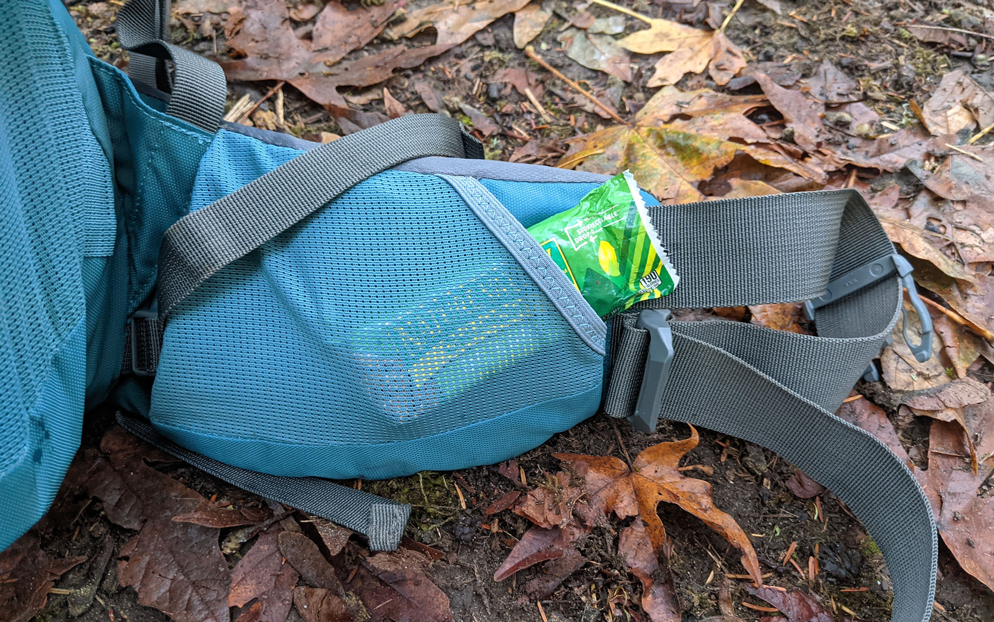 A granola bar sticks out of the Coyote's right hip belt mesh stretch pocket.