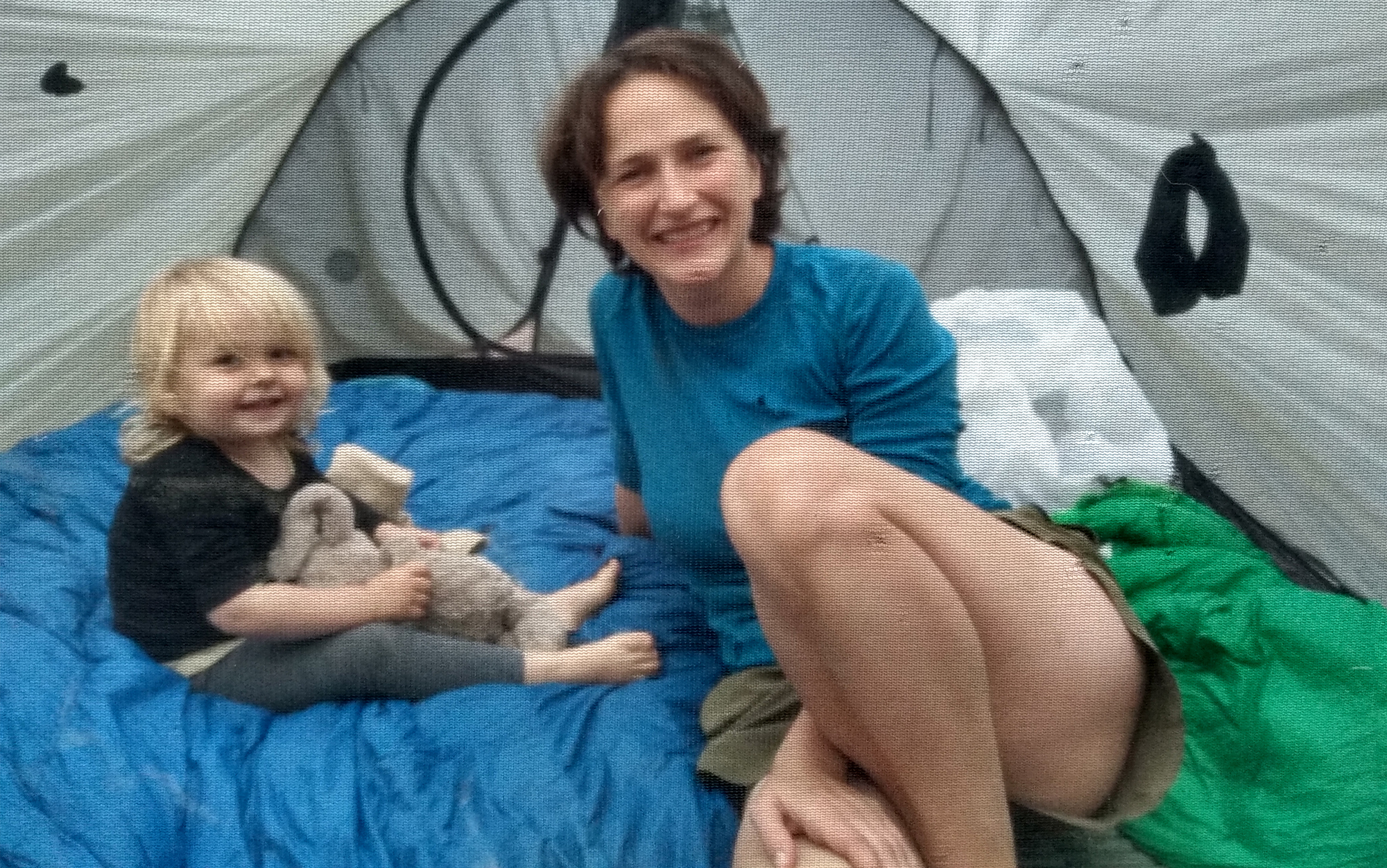 A woman and child are sitting on quilts in a tent.