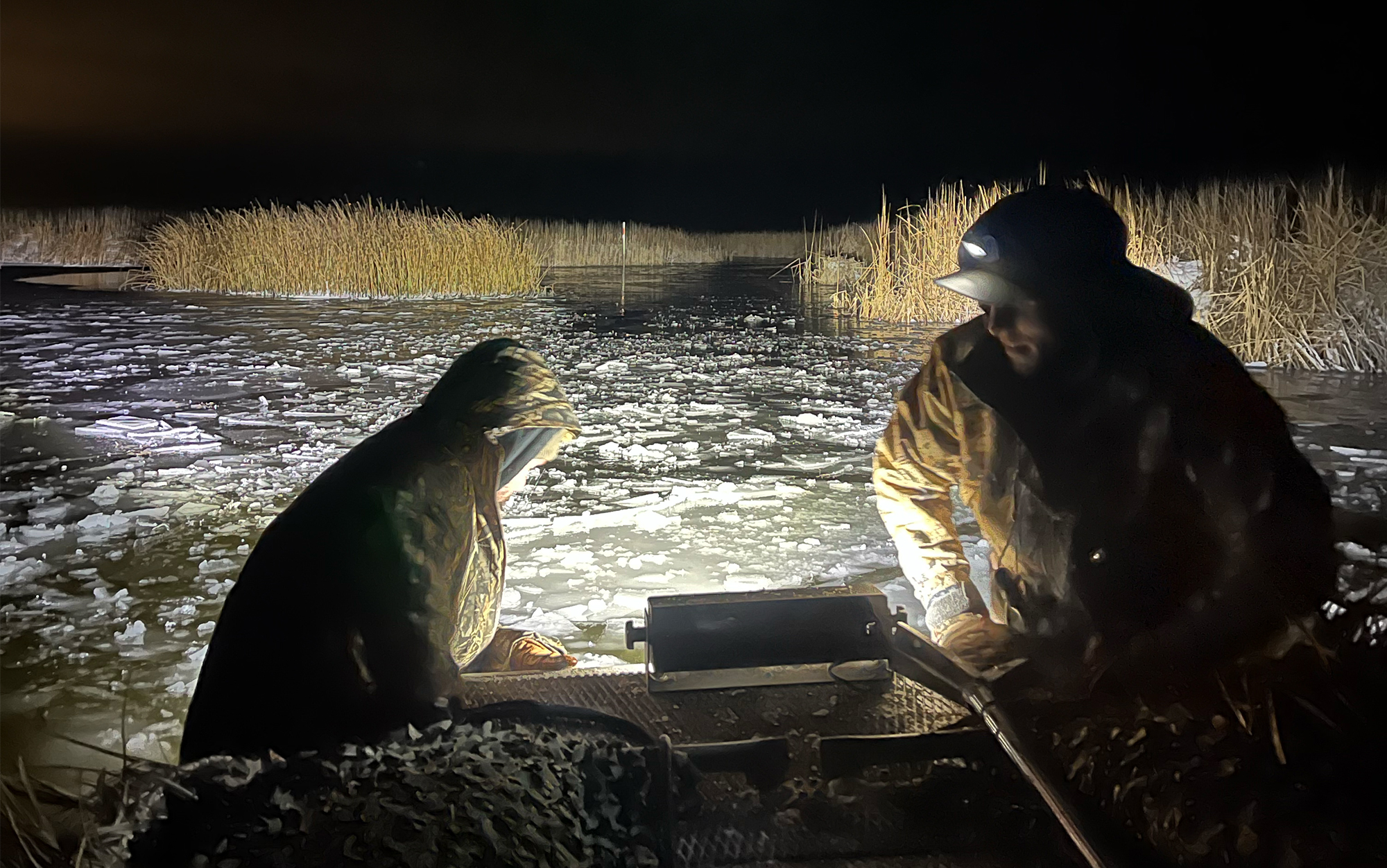 Deux chasseurs de canards cassent la glace devant le bateau.