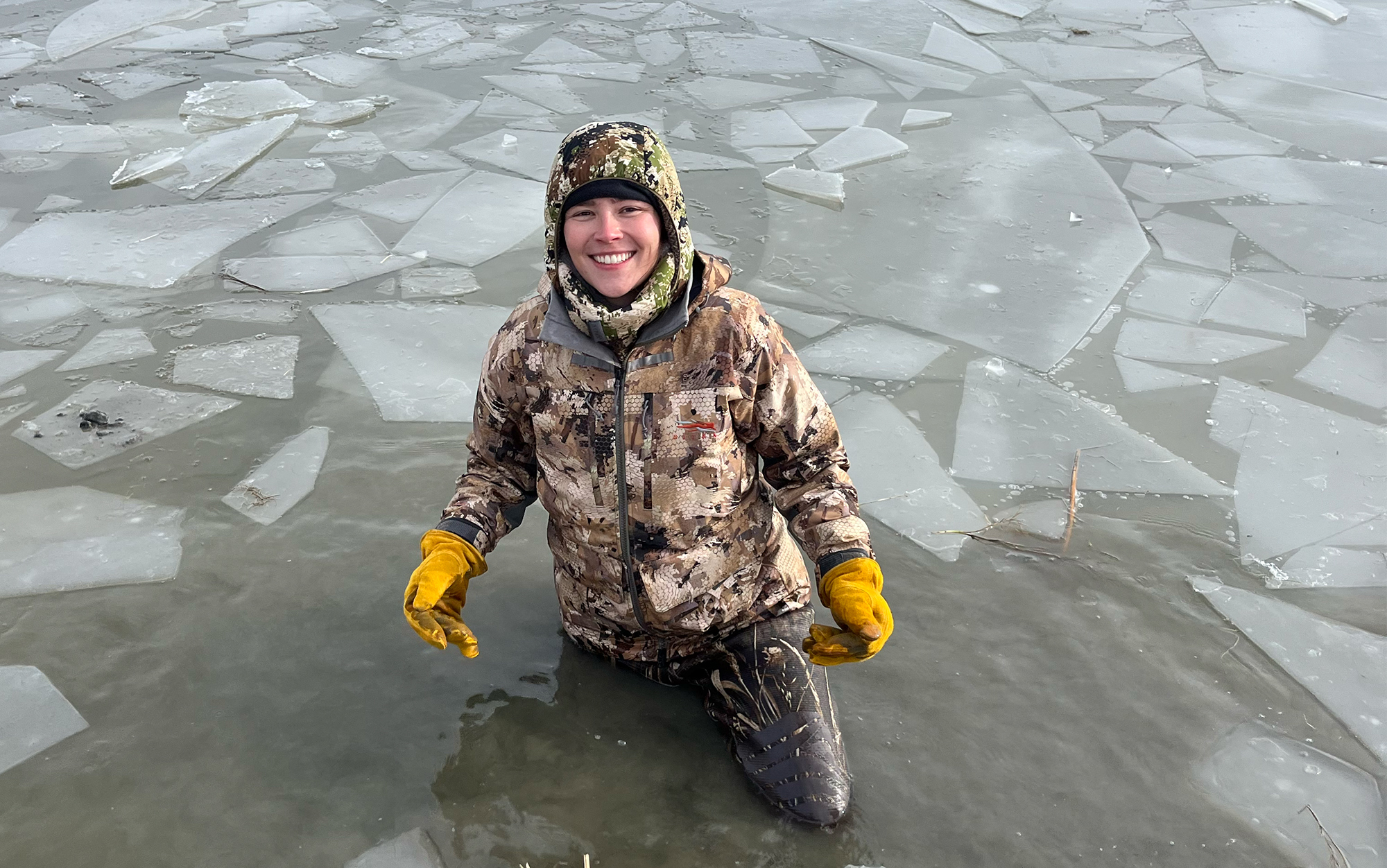 Duck hunter wearing Sitka Hudson jacket in icy bay.