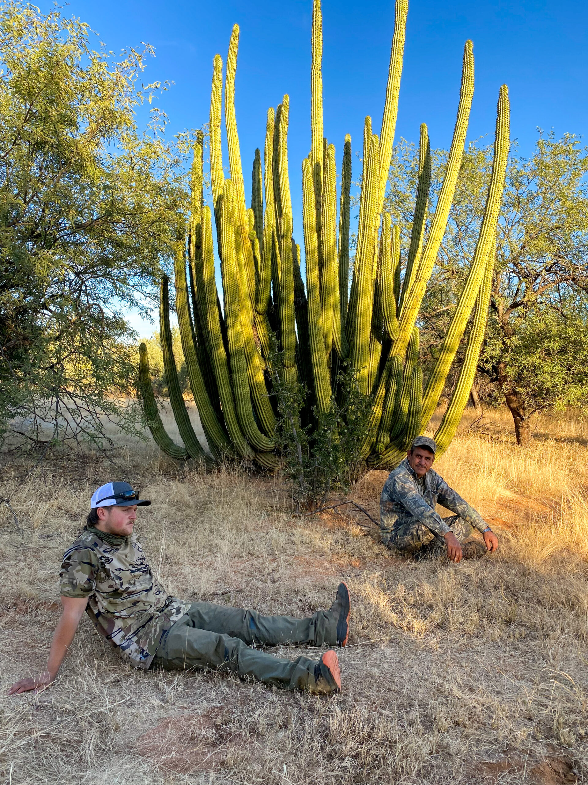 Two hunters relax near a large cactus