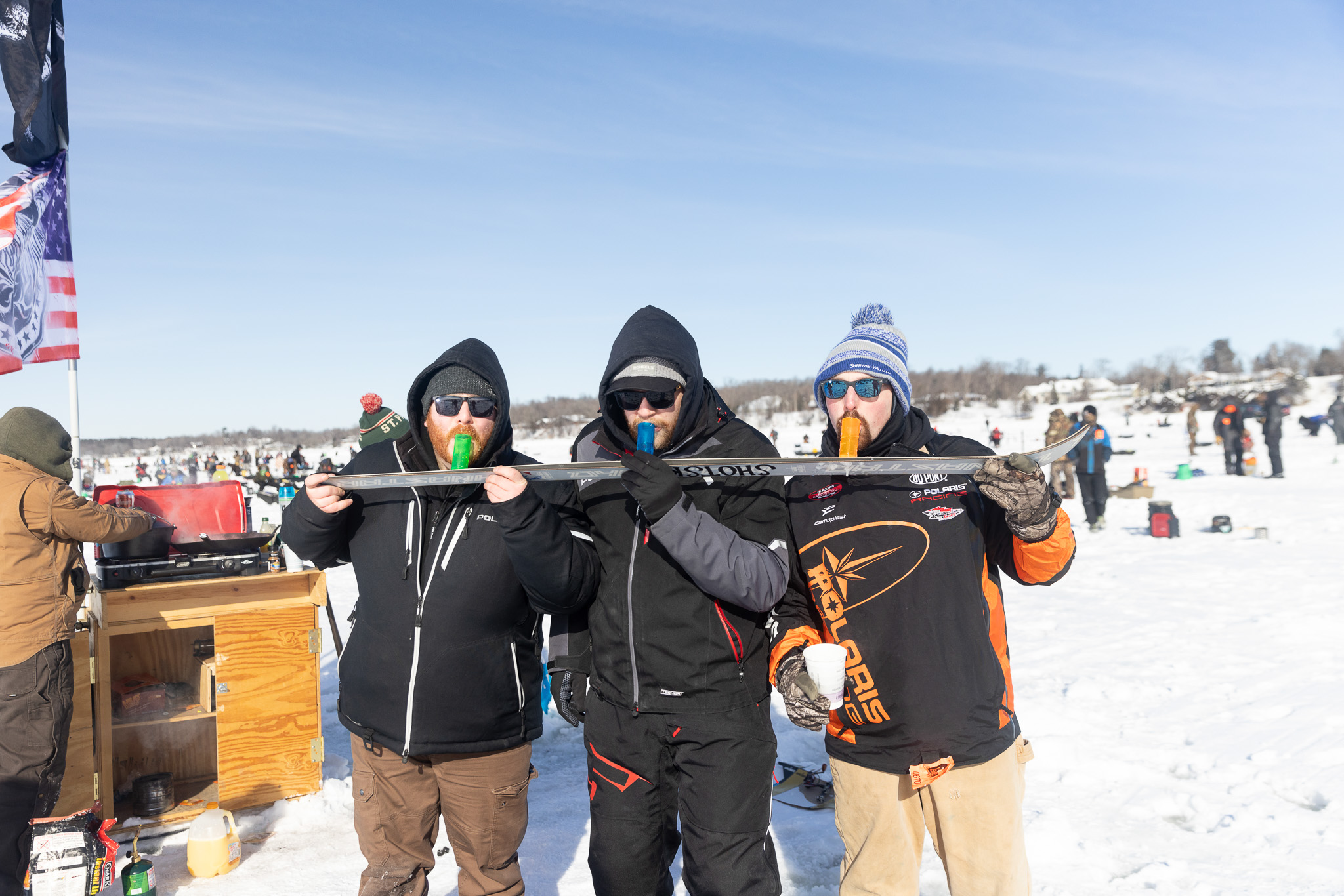 Three men prepare to tip back a shotski while ice fishing.