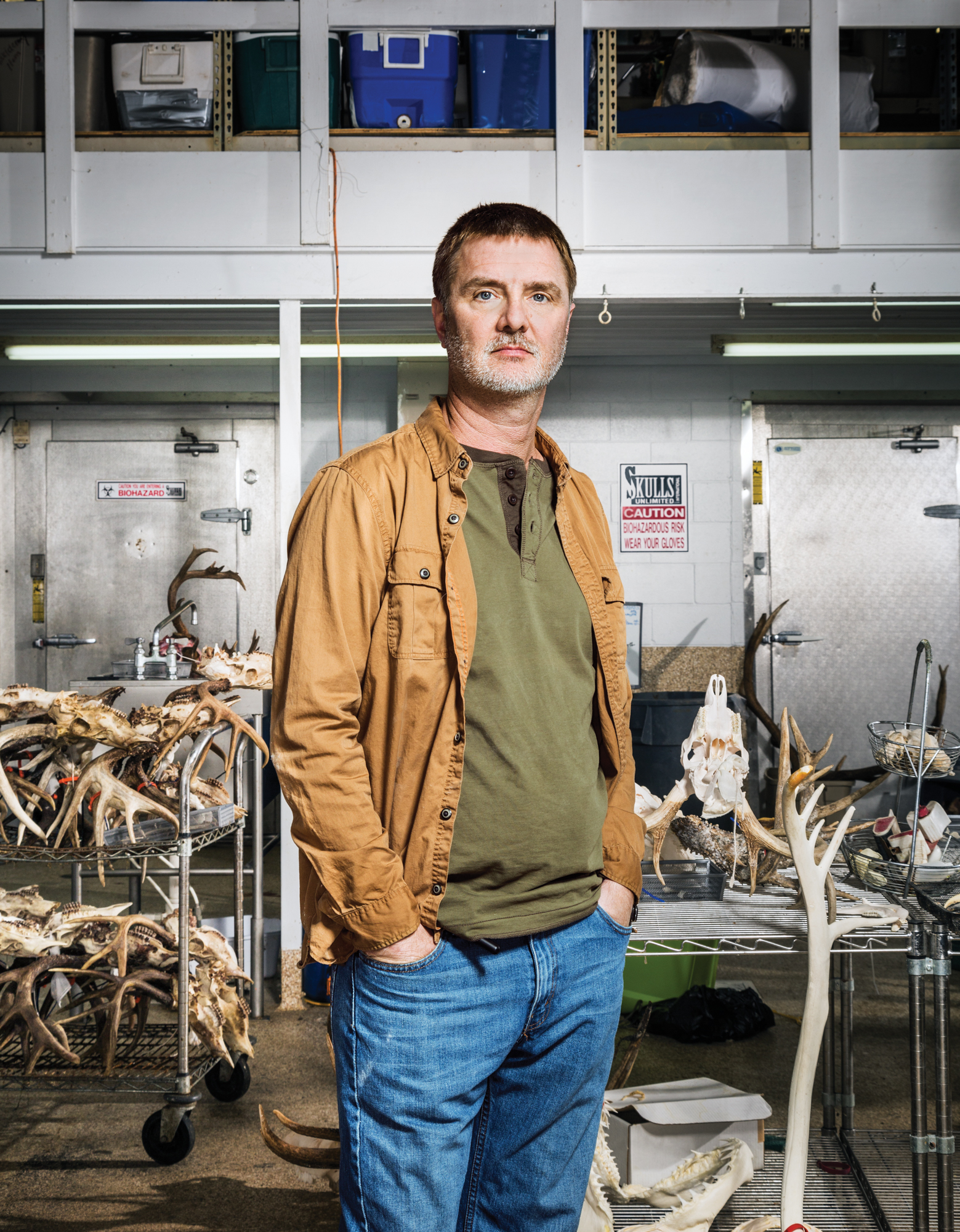 A man stands with his hands in his pockets in front of work tables at a taxidermy shop.