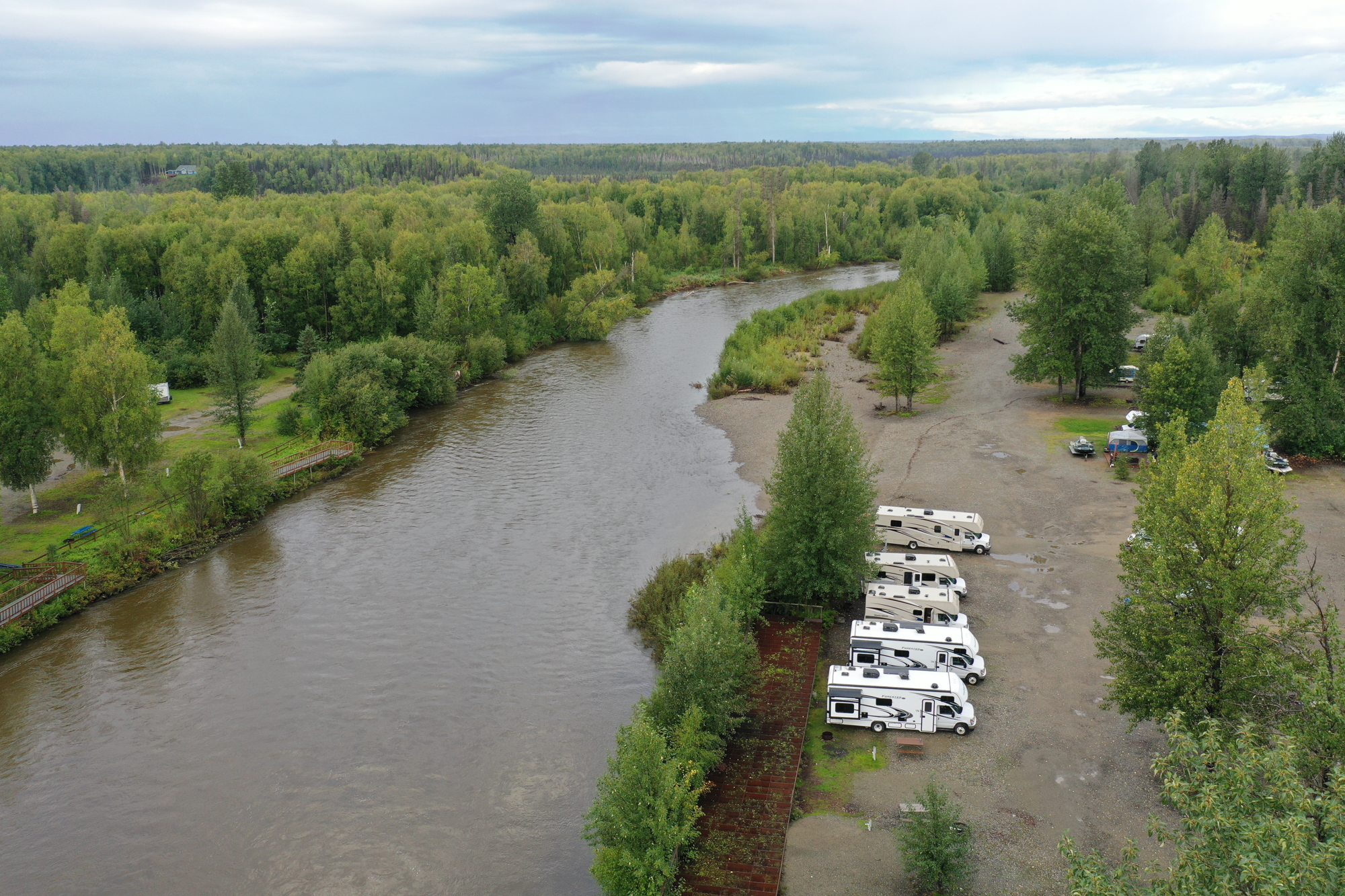 A row of five RVs lined up along a stretch of river in Alaska.
