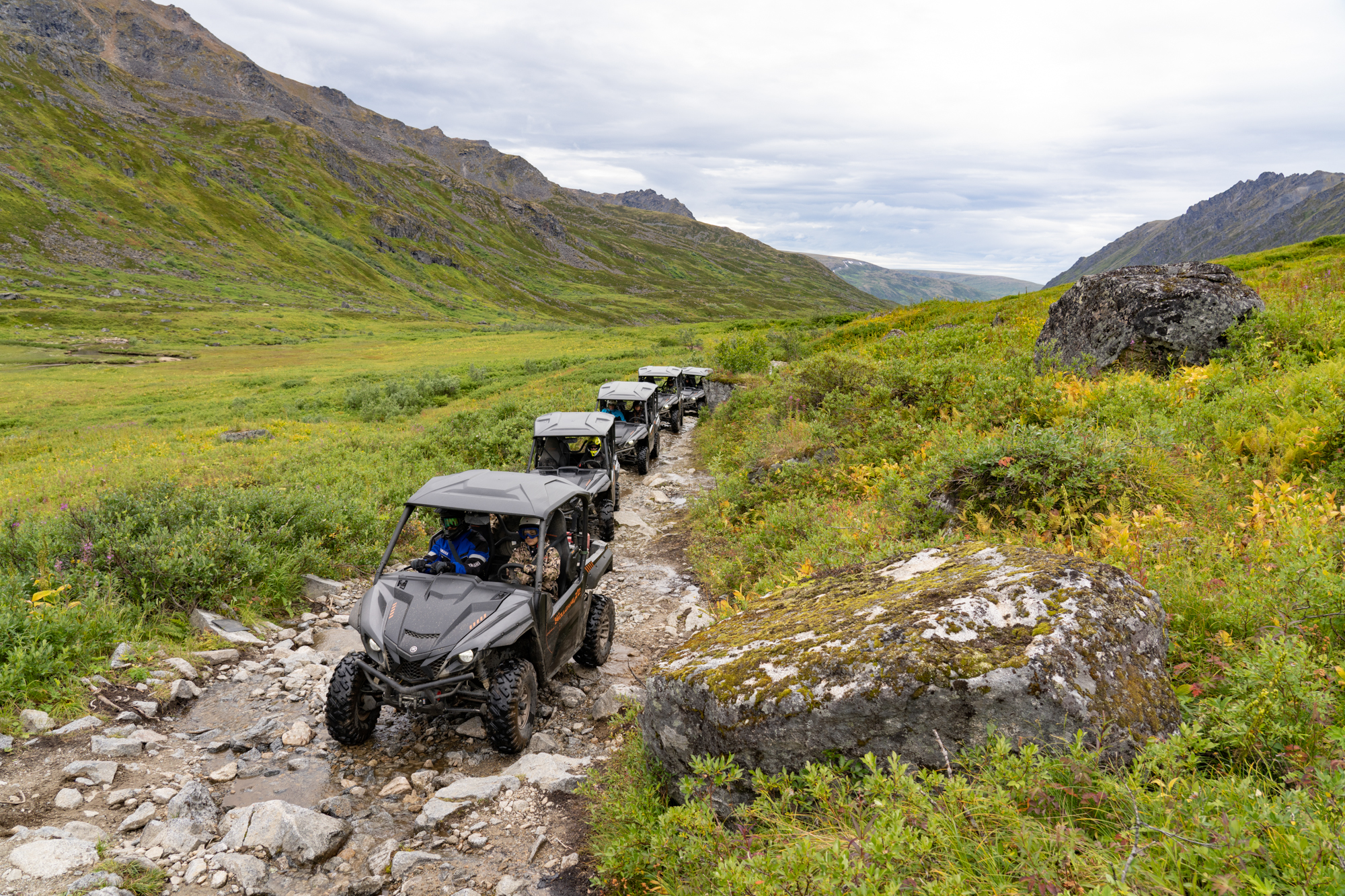 A line of Yamaha Wolverine UTVs crawl over a rock trail in the Talkeetna Mountains of Alaska.