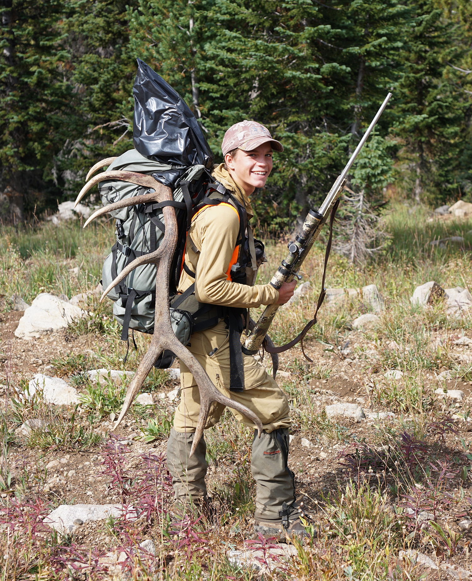 Young hunter carries rifle and elk antlers.