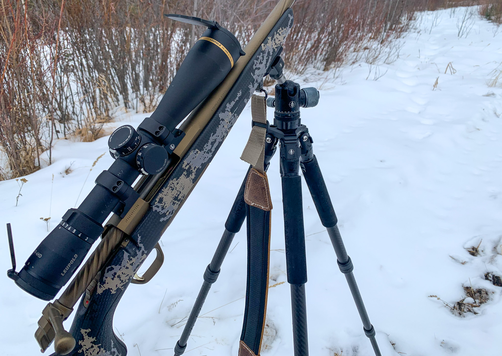 A Browning rifle with a Leupold scope sits on a tripod in the snow.