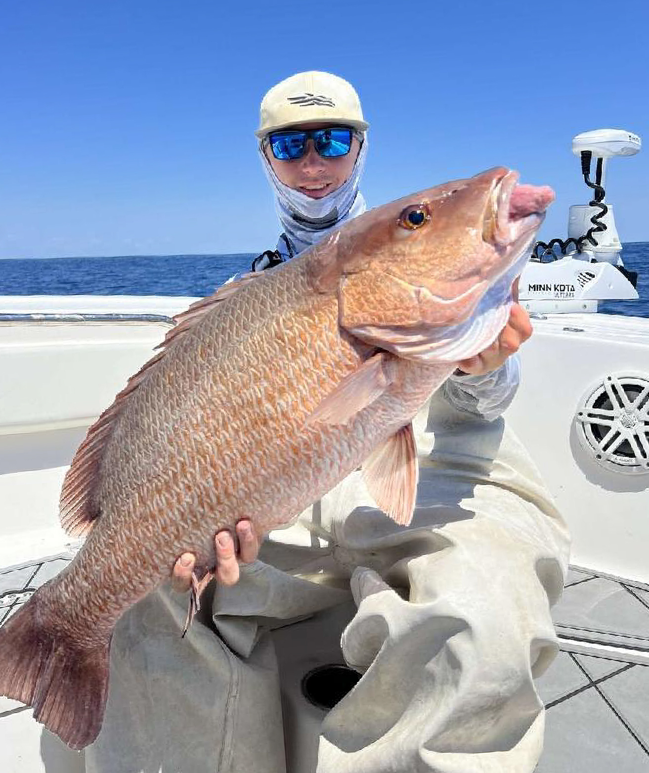 An angler in a hat and sunglasses holds up a fat snapper.