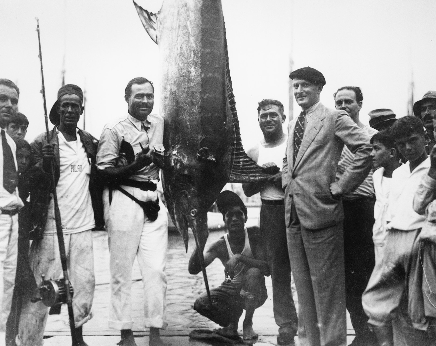 historical photograph of ernest hemingway, huge marlin, and crowd at the marina in cuba.