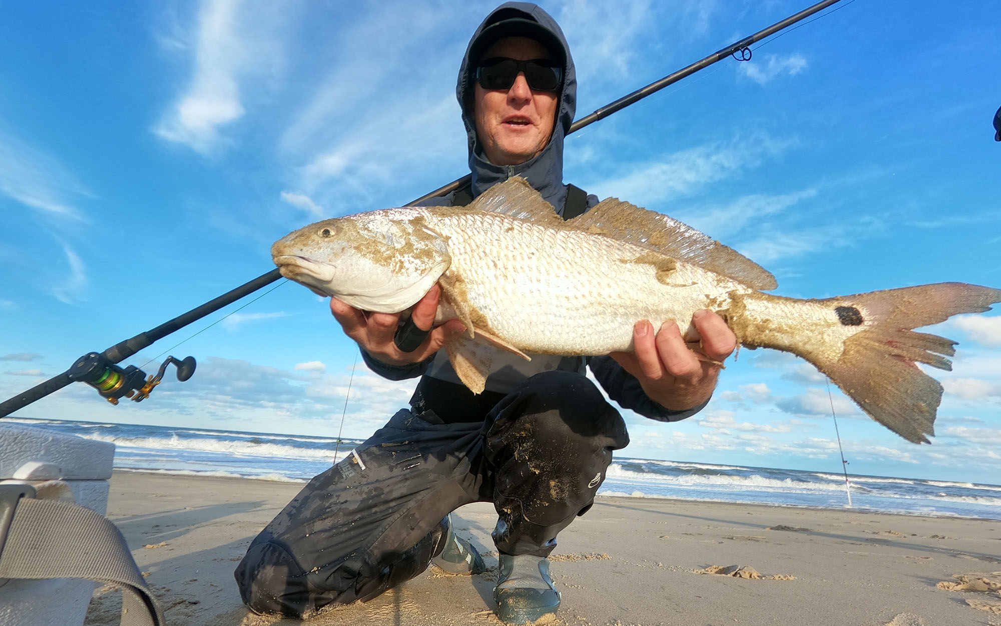 Angler holds fish on a beach.