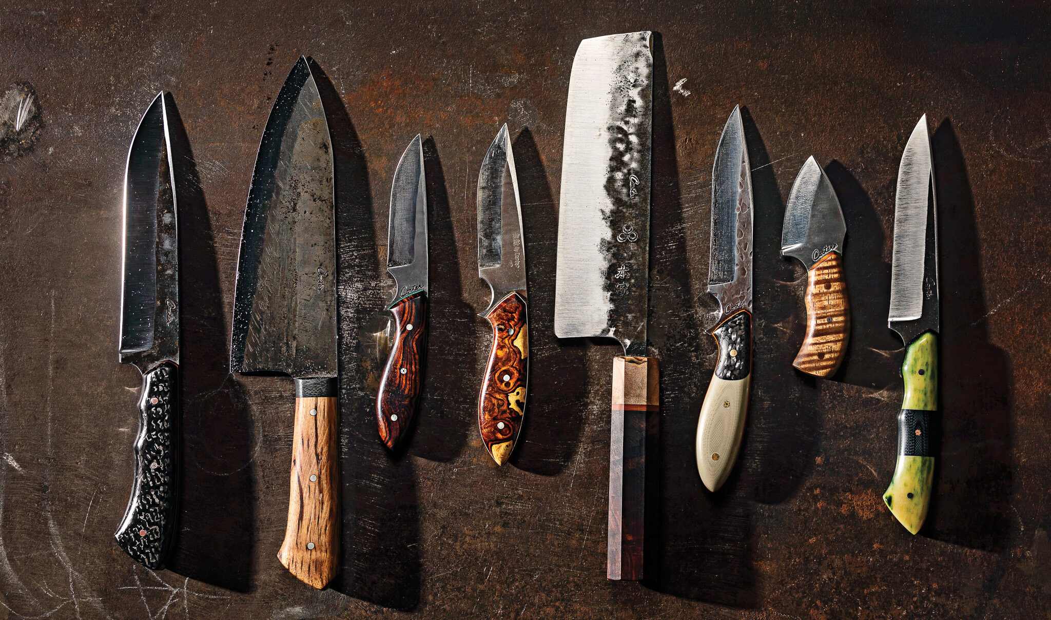 A collection of knives handmade in Portland lined up on a table.