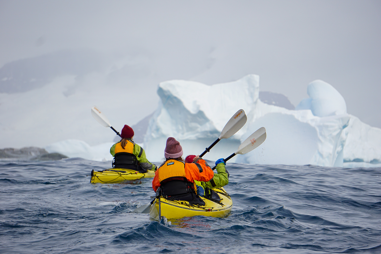 kayakers in two boats approach an iceberg