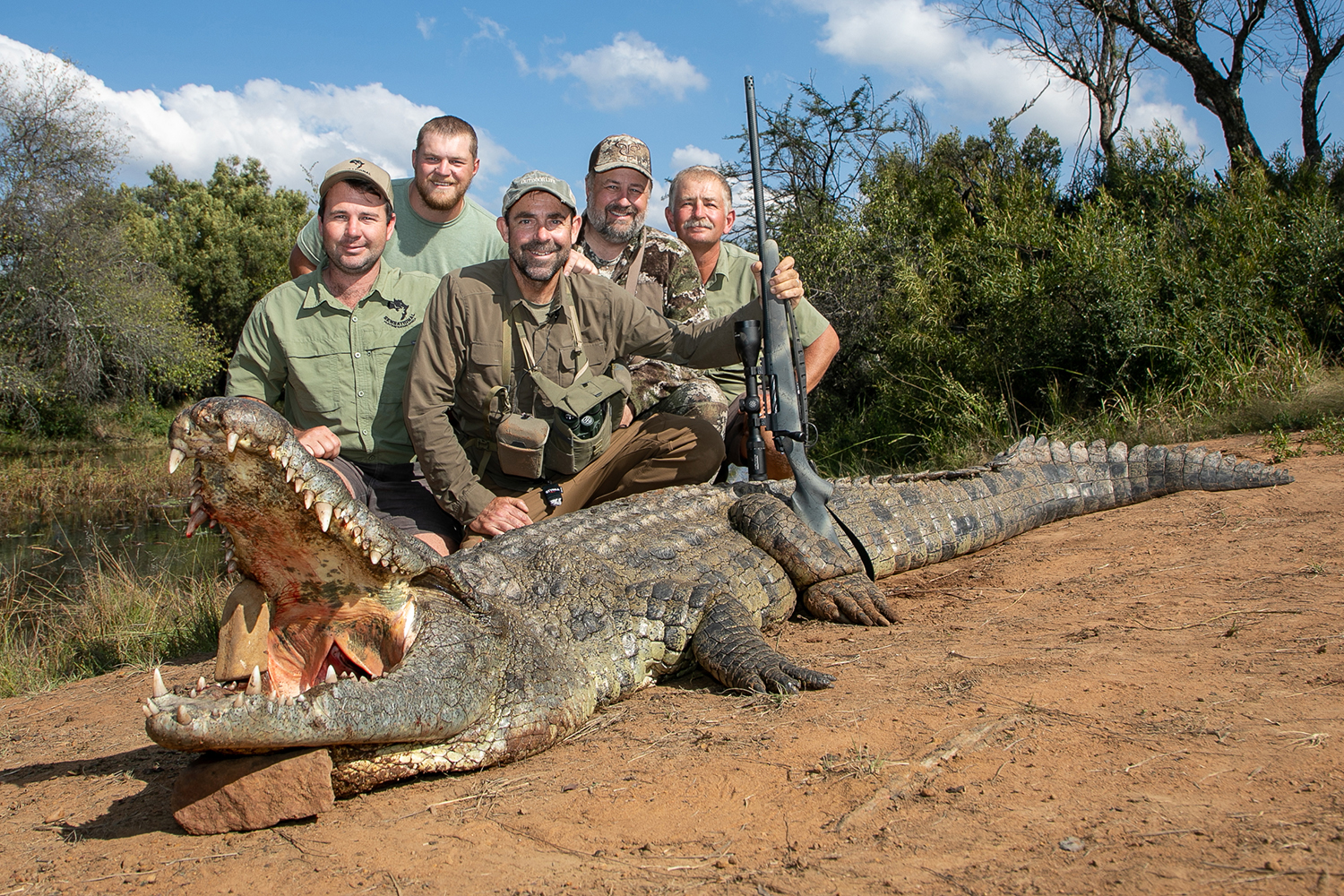 five hunters pose behind crocodile