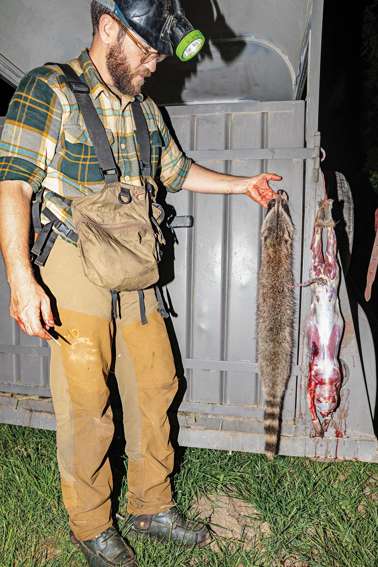 hunter holds up pelt and views skinned raccoon
