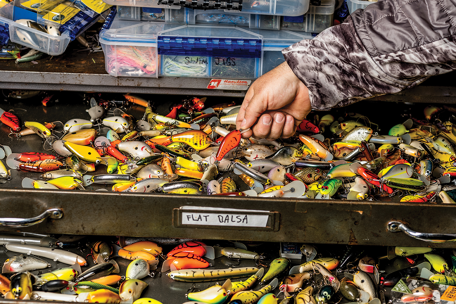 hand reaches into a drawer full of fishing lures; label reads "flat balsa"