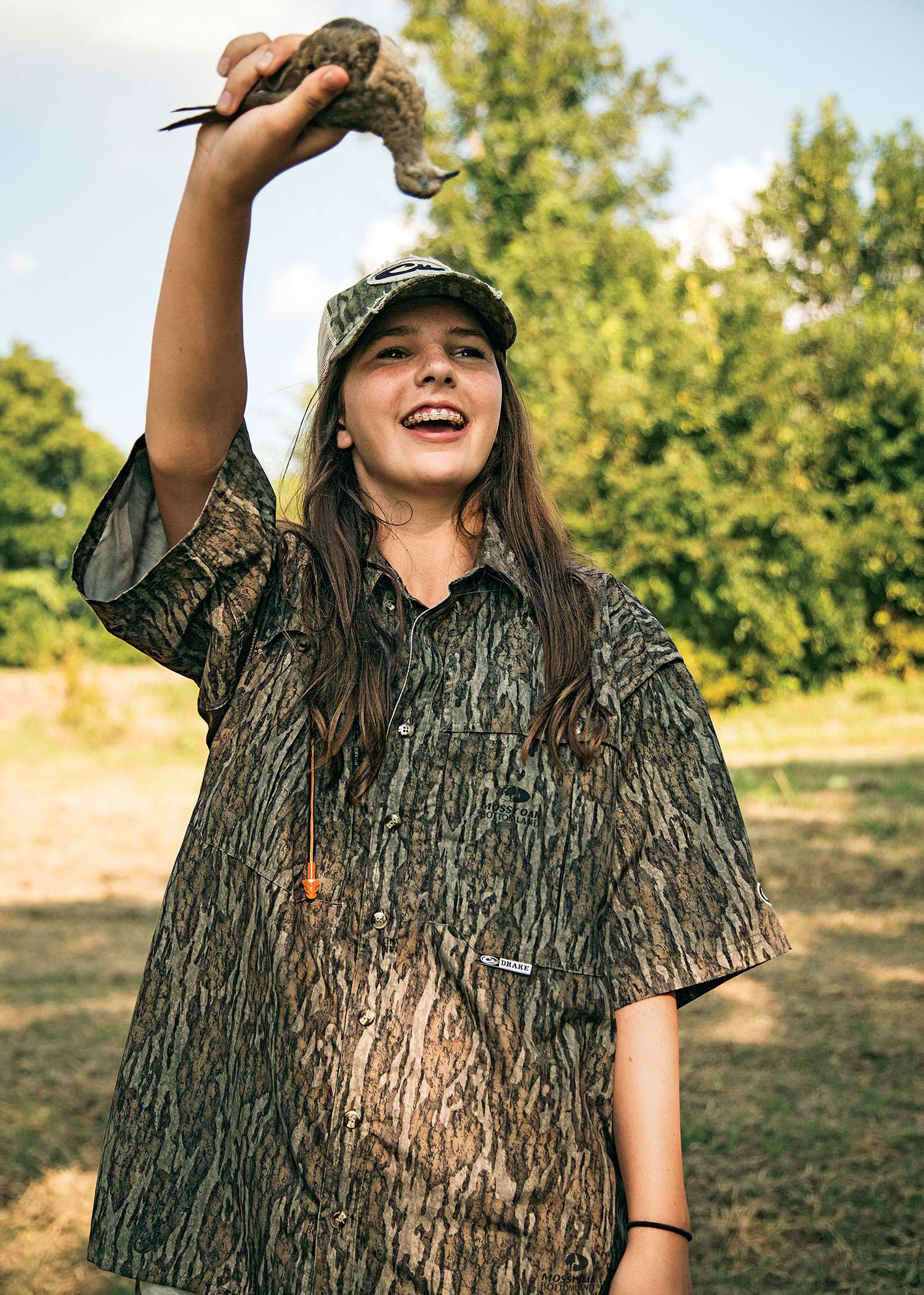 young woman in camo shirt and cap holds up dove