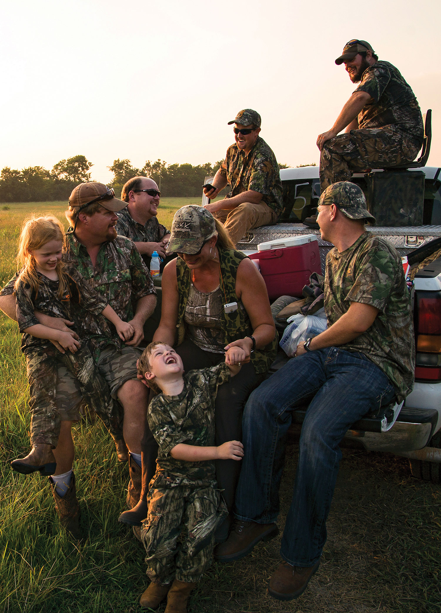 group of adults and children wearing camo gathers on open bed of pickup truck