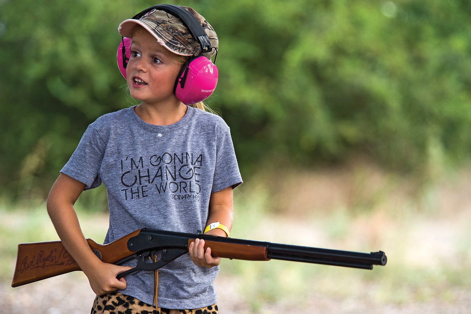 Young hunter with pink ear-protection muffs and camo hat holds pellet gun