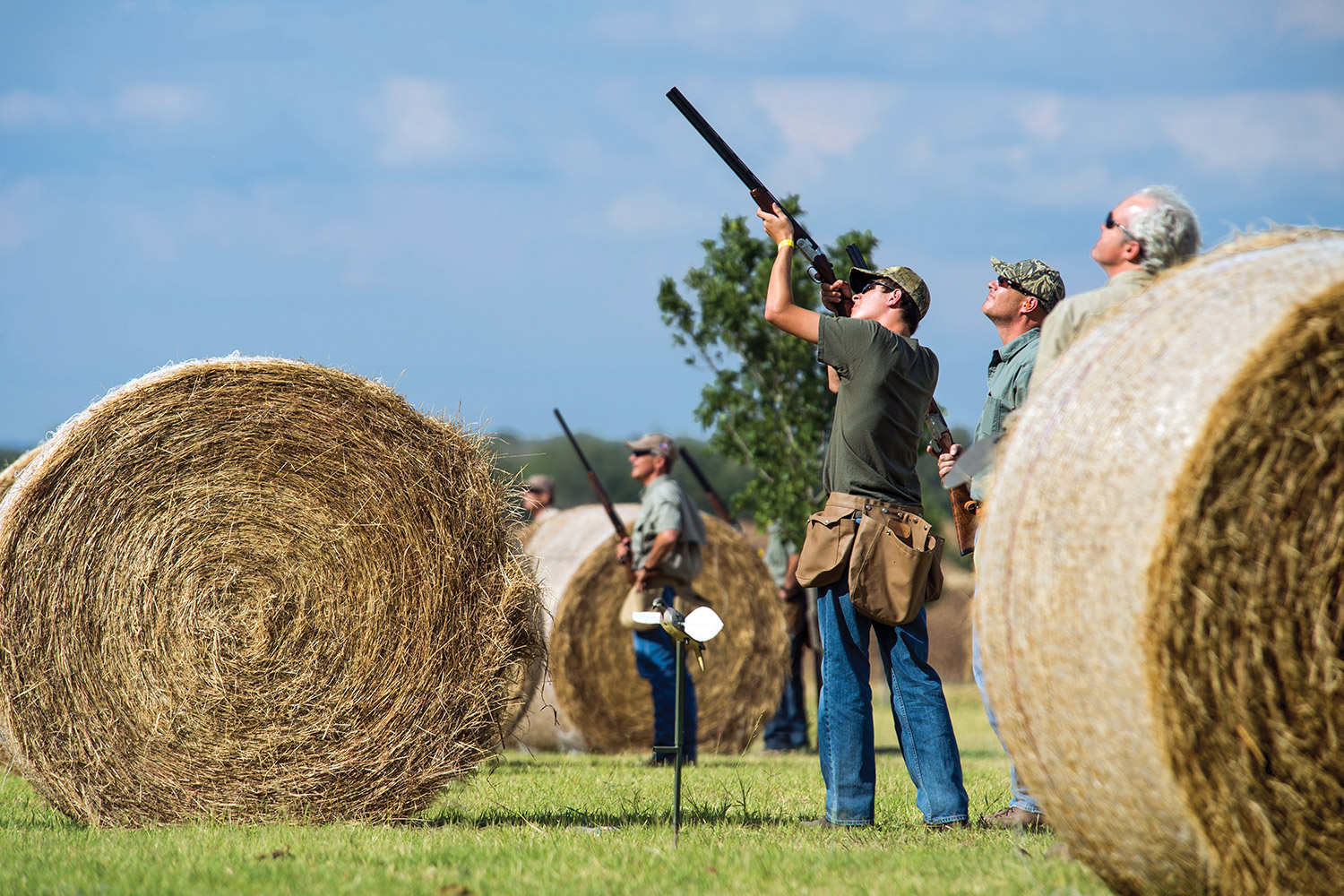 Dover hunter shoots from station behind rolled hay bale as others watch.