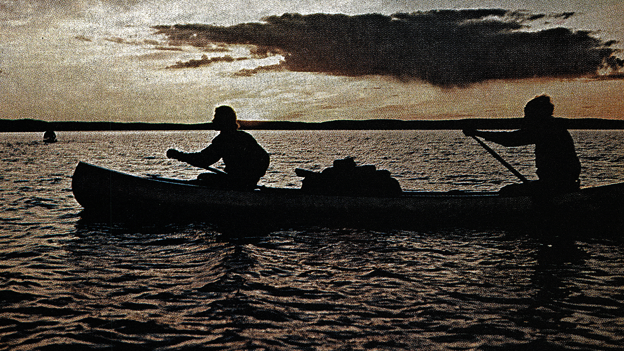 silhouette of two canoeists paddling across lake mostly in darkness
