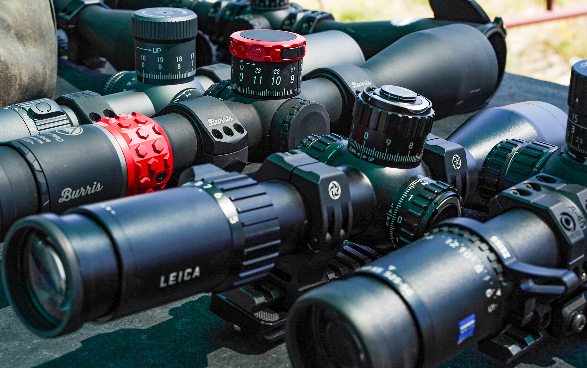 Leica and Burris long range scopes sit in a line.