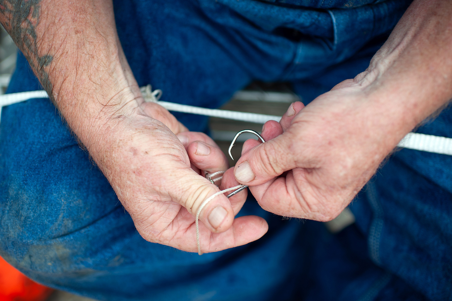 closeup of hands tying a fishhook to a line