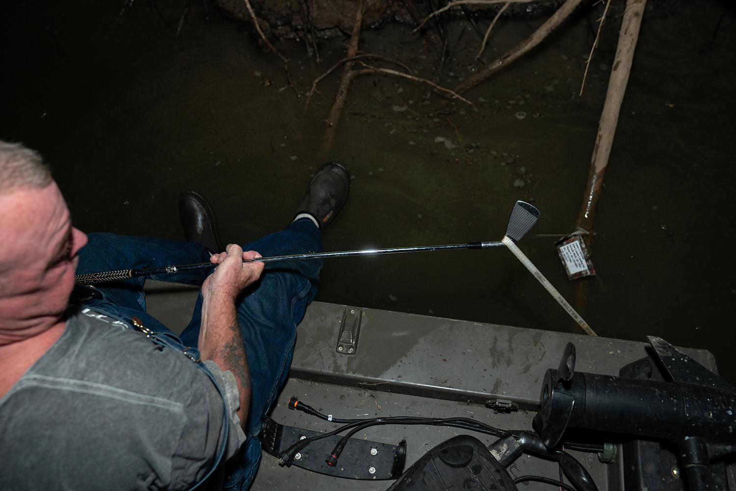 man uses golf club to lift trotline from river