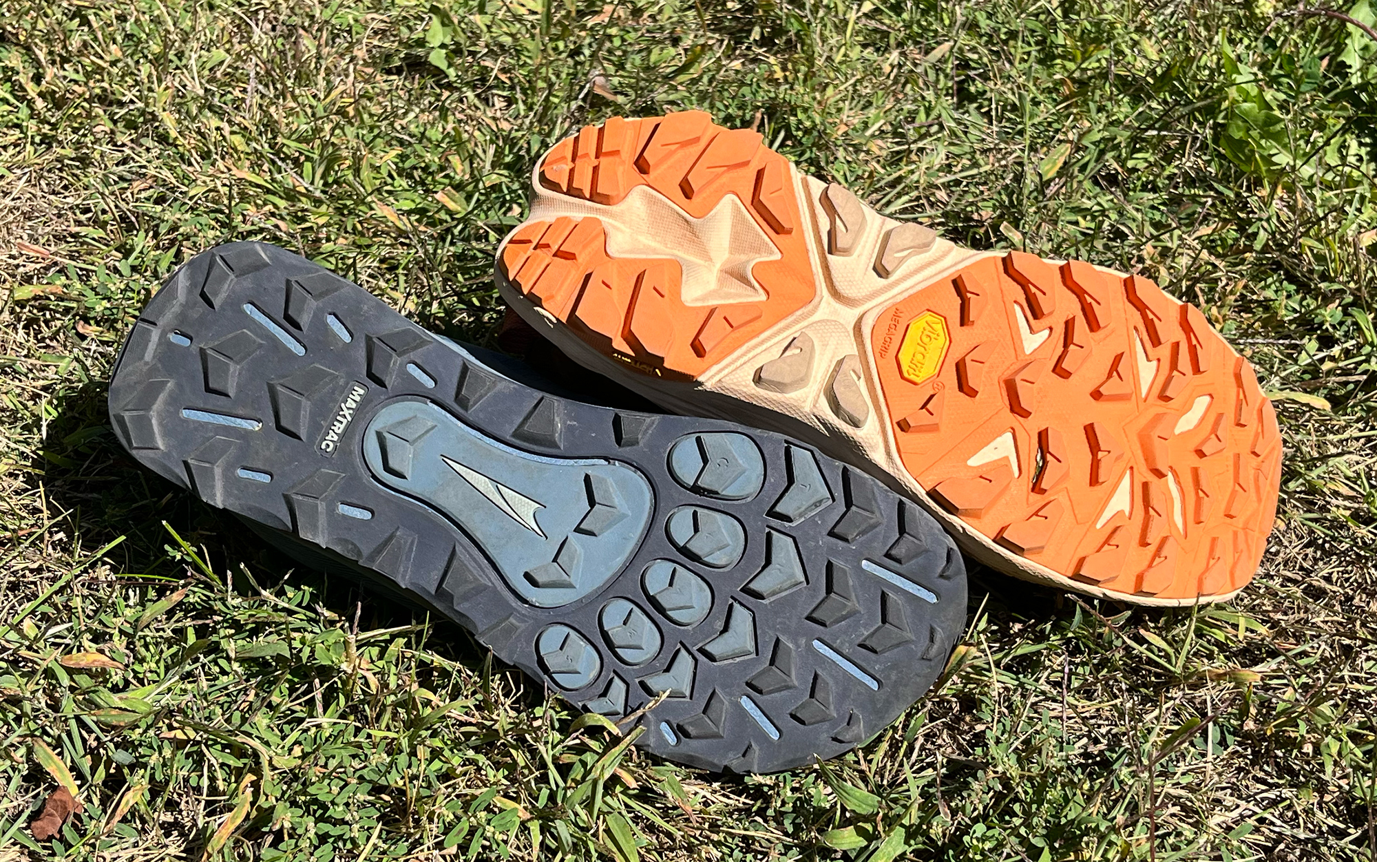 The Altra Lone Peak and Hoka Anacapa sit upside down in the grass.