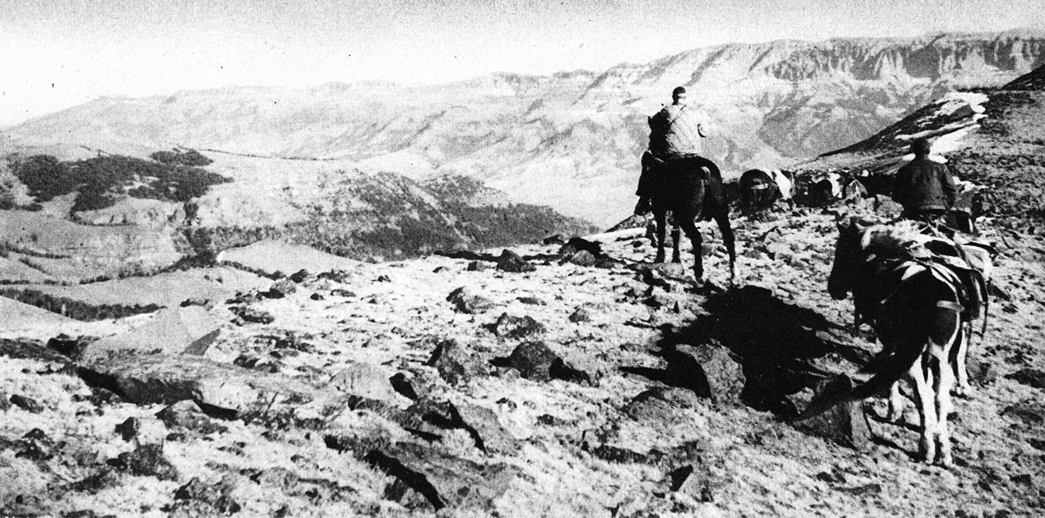 two hunters on horseback crest ridge overlooking big valley