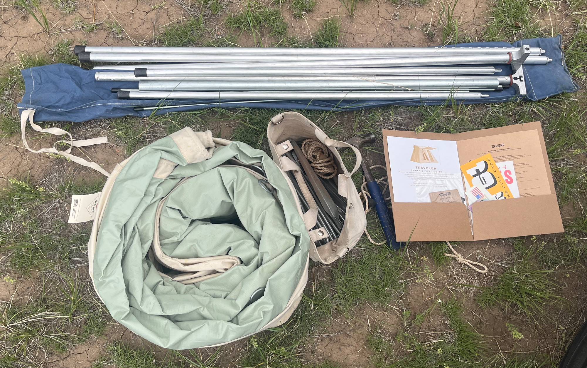 Pictured is the Traveler tent with storage bag, pole set with storage bag, tent stakes in the included canvas bag with awning ropes, the ownerâs field guide, and a hammer.