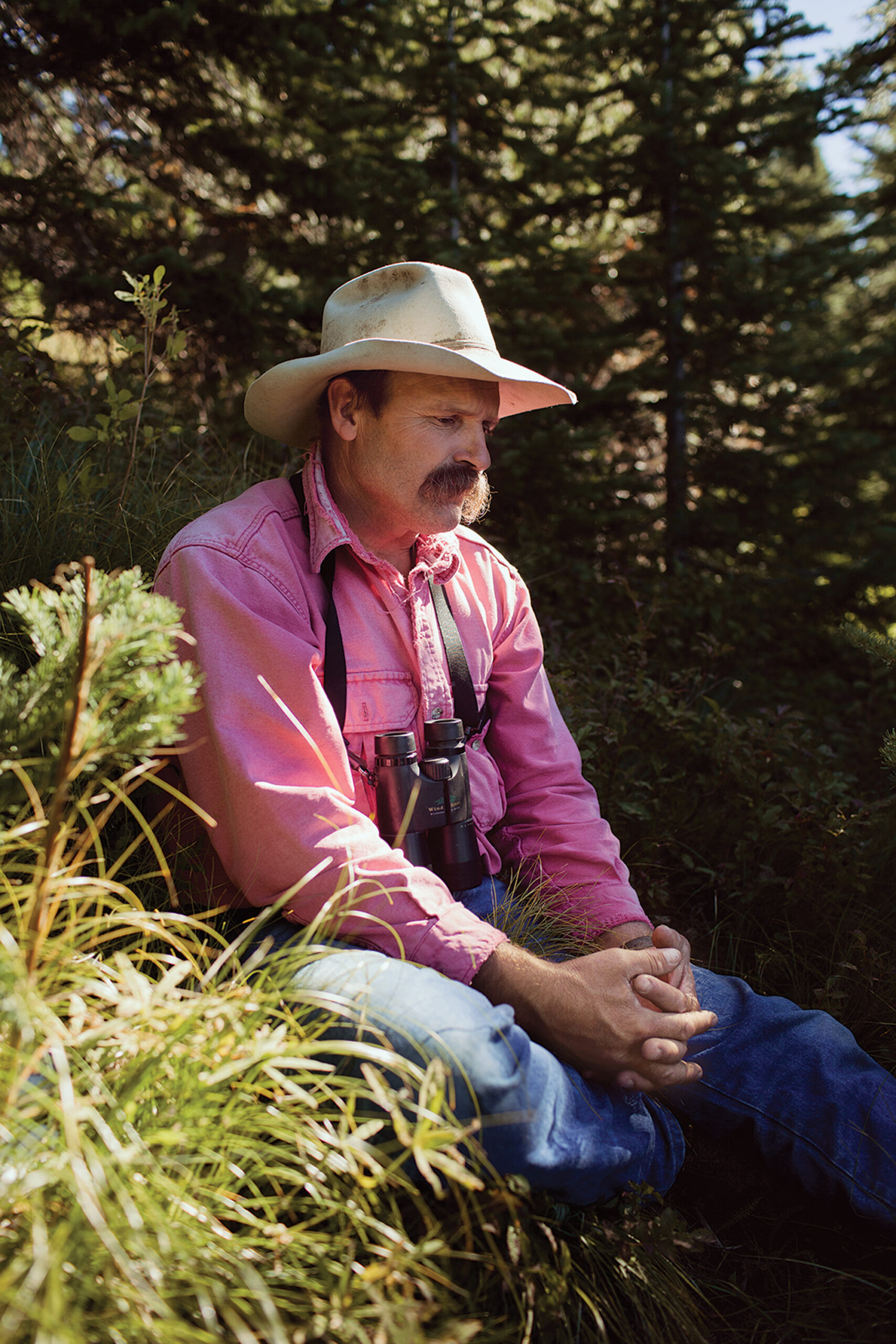 A hunter in a cowboy hat and red shirt reflects after a day of bear hunting.
