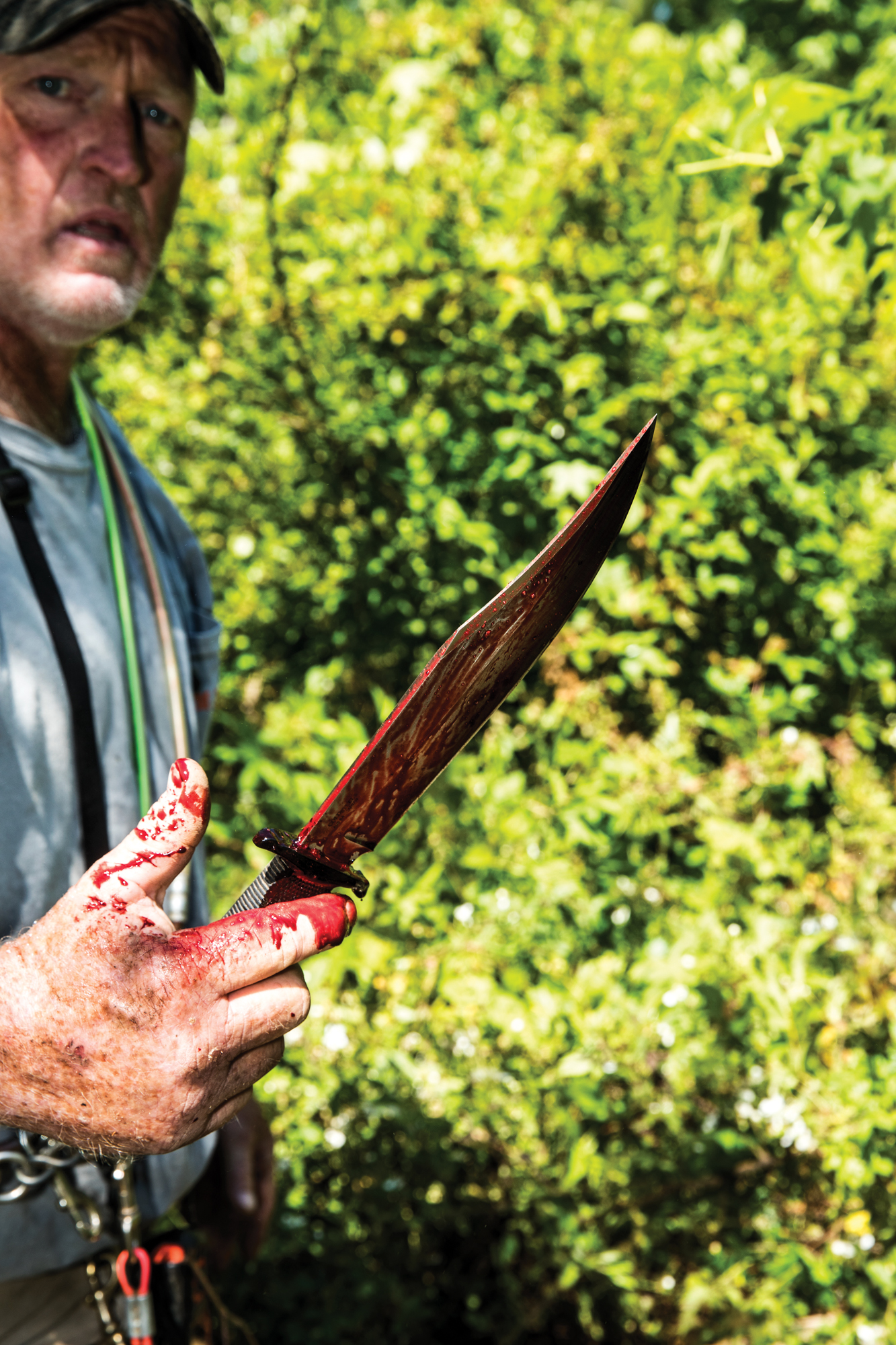 A hog hunter holds a bloody knife.