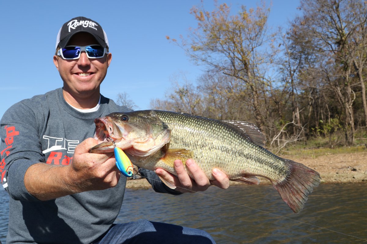 a man holds up a bass caught from muddy water.