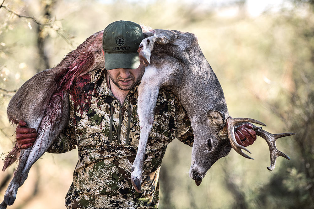 hunter hauling coues deer over his shoulders