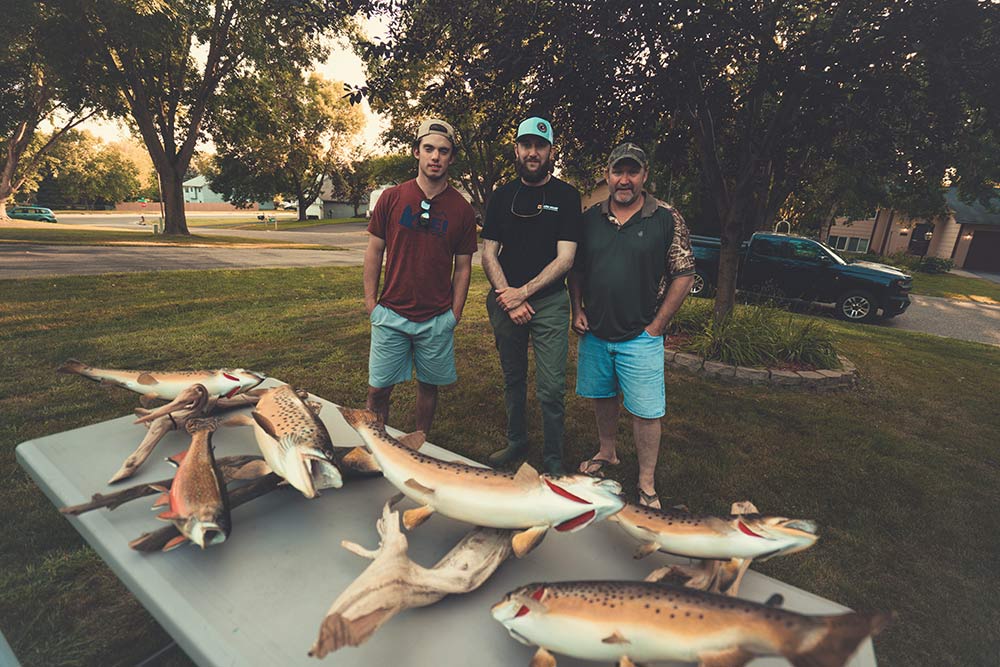 three men standing behind trout trophies