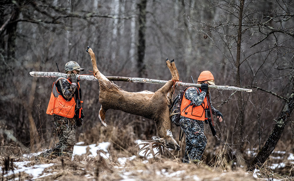 two hunters hauling whitetail through woods