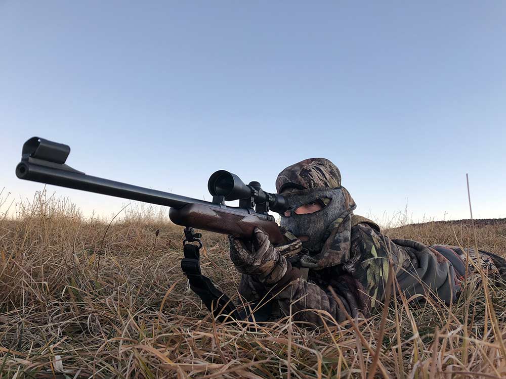 young hunter aiming rifle while laying on the ground
