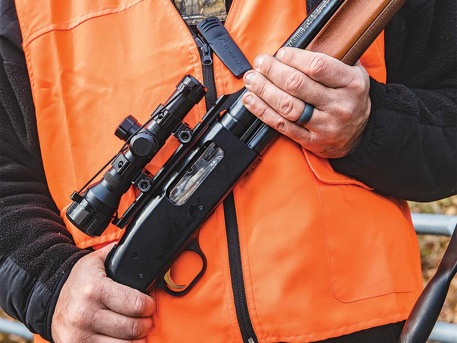 a hunter wearing an orange vest and holding a rifle