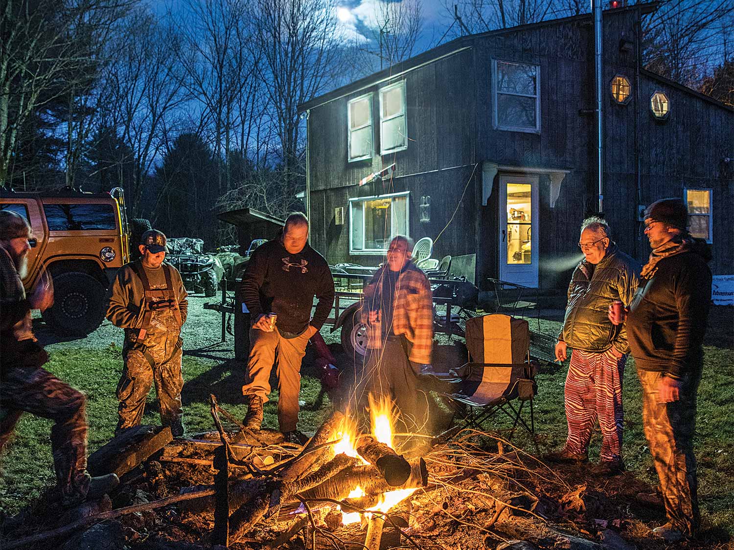 group of hunters standing beside a fire at deer camp during the night
