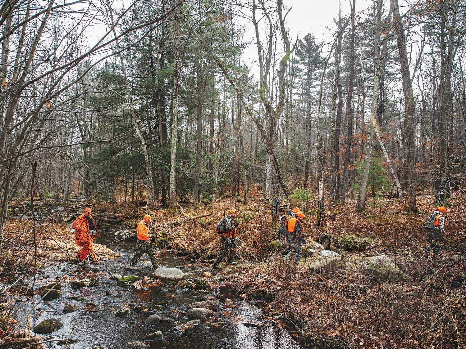 four hunters crossing a creek in the woods