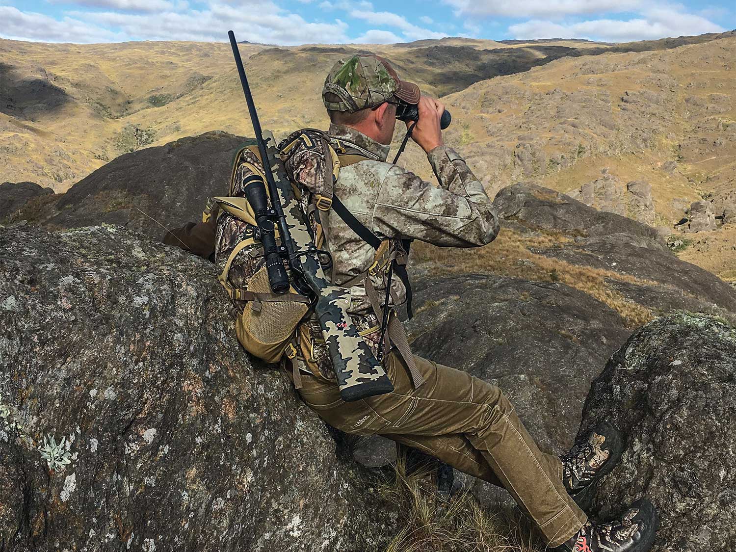 hunter sitting on a rock while looking through binoculars