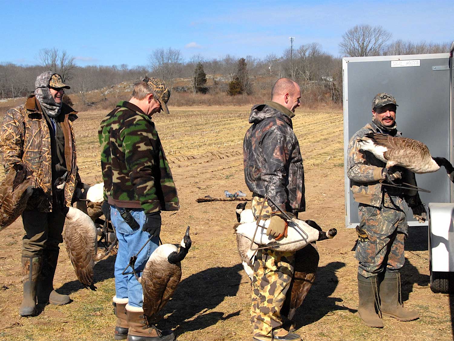 four bird hunters holding goose decoys