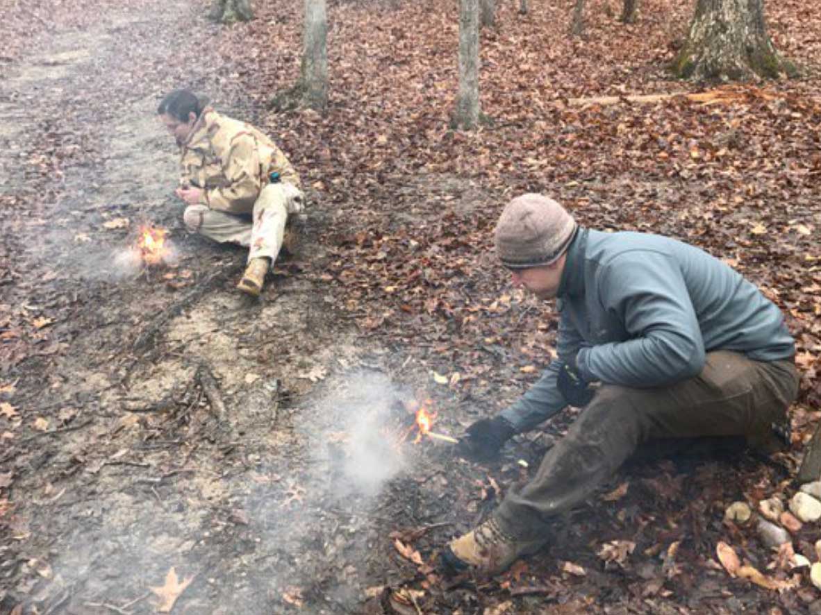two men practicing building a fire in the woods