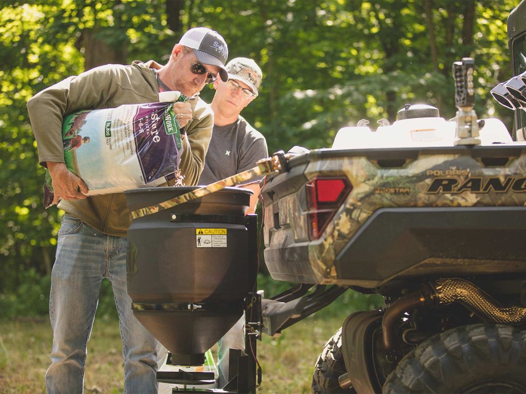 men adding fertilizer to utv dispenser