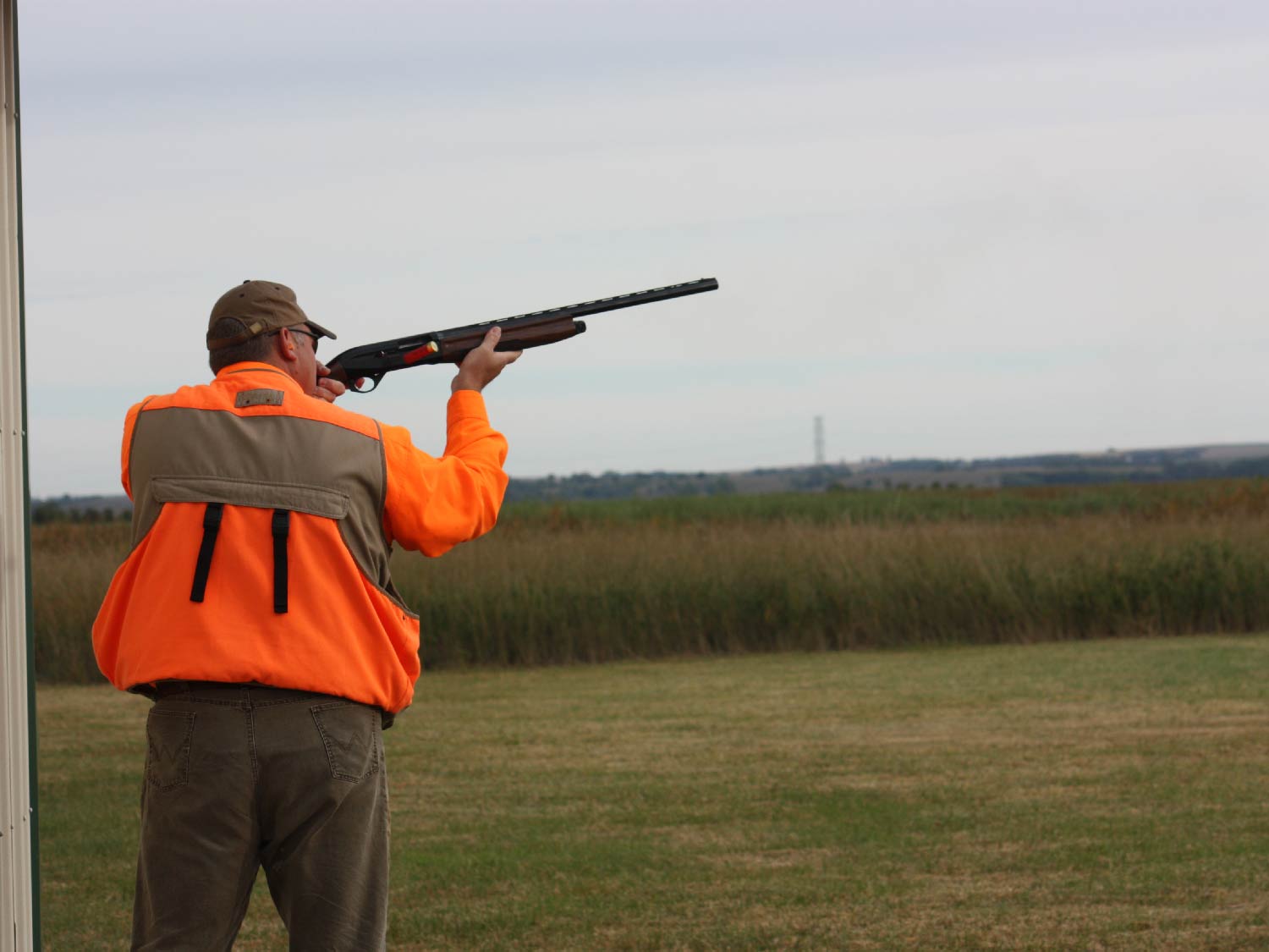 man aiming a shotgun in a field