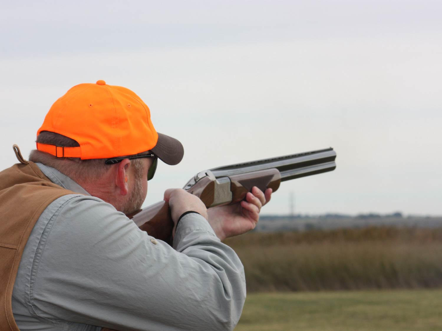 man aiming a shotgun in a field