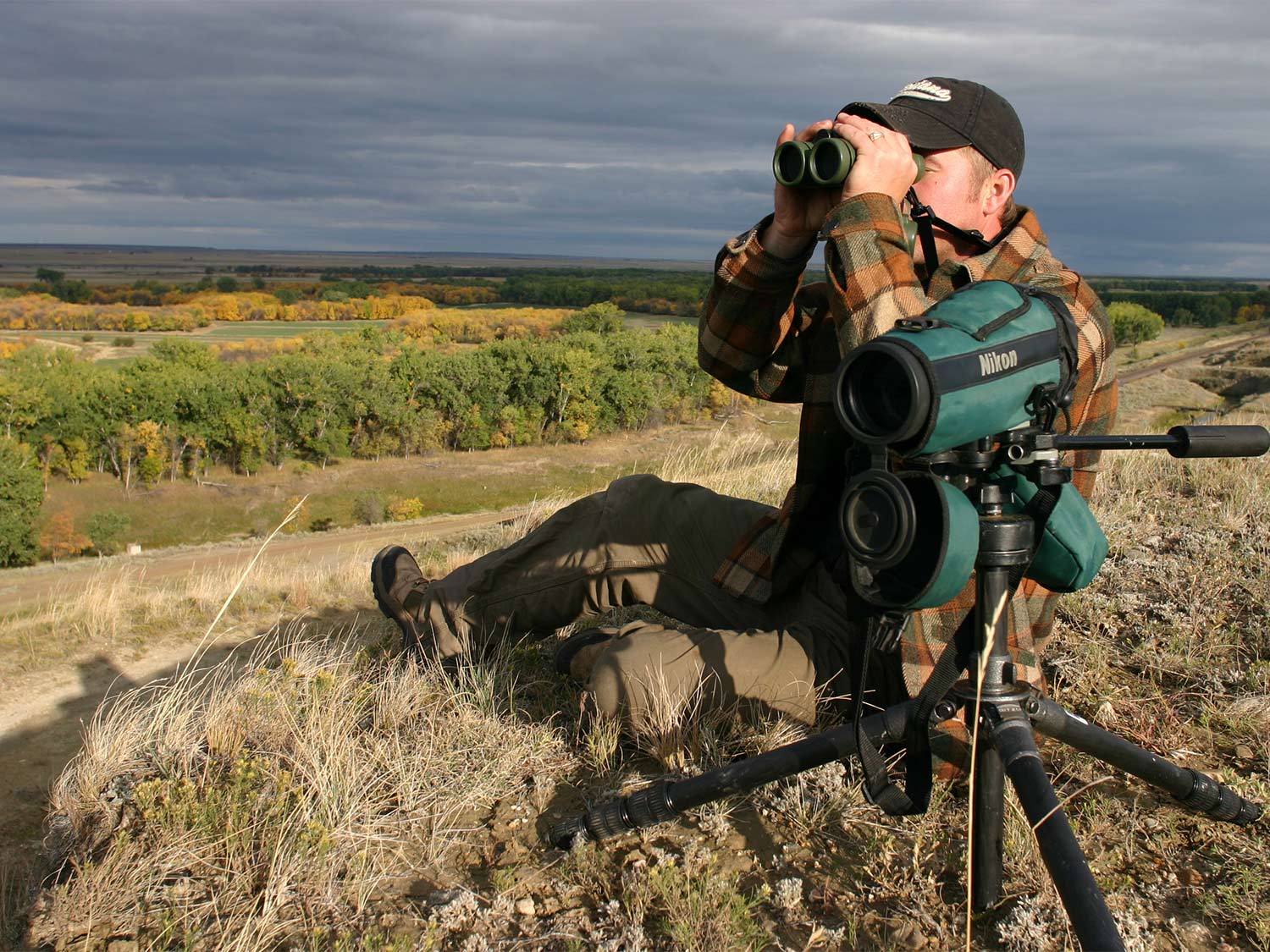 hunter sitting on the ground looking through optics