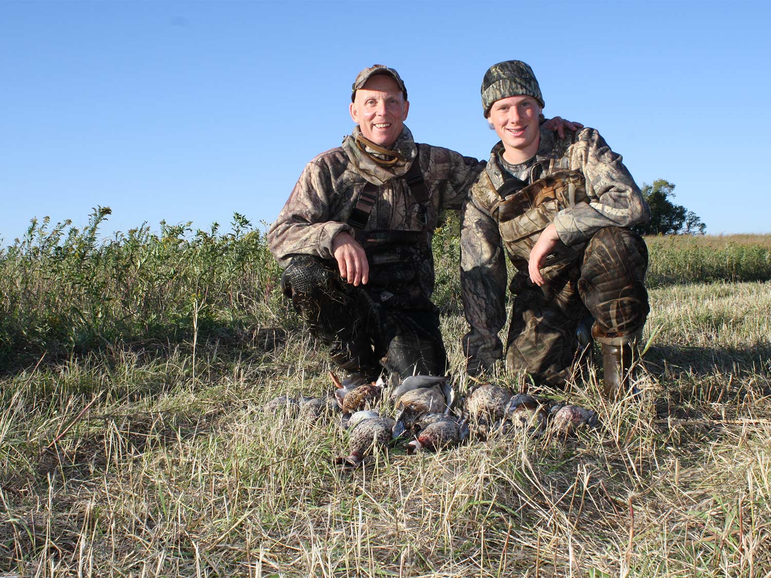 two hunters kneeling behind ducks