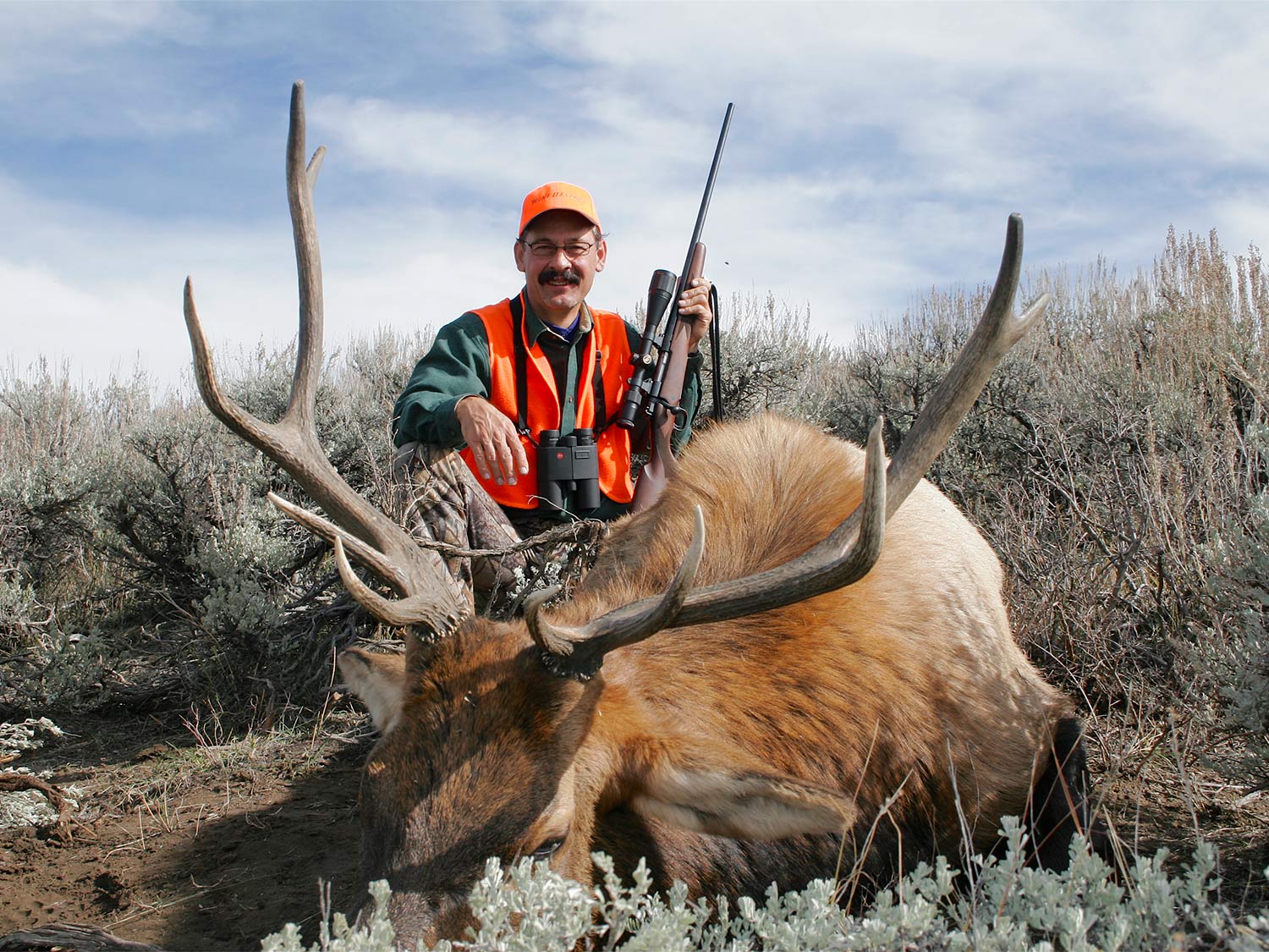 hunter kneeling behind a giant bull elk