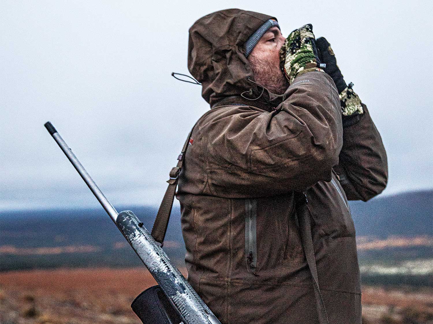 a hunter with a rifle on his back while he bellows out a moose call